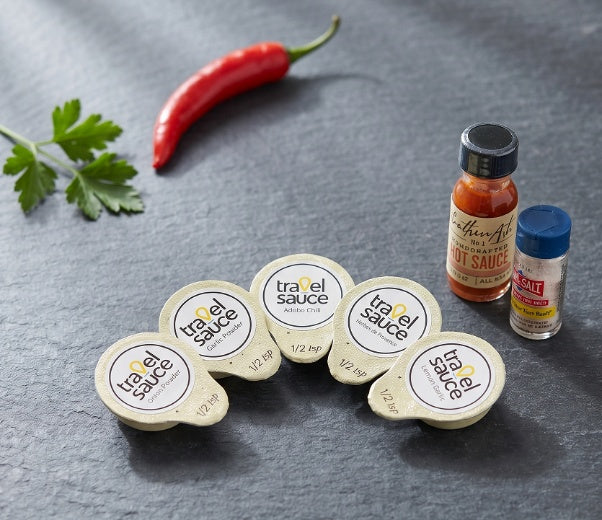 Travel Sauce spice pods with chili, fresh herbs, hot sauce and salt on slate